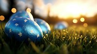 Blue Christmas ornament with silver stars nestled in green grass at sunset, with golden bokeh lights creating magical holiday atmosphere outdoors.