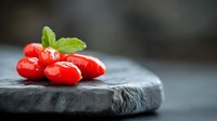 Fresh red cherry tomatoes with green basil leaf on dark slate stone board for culinary cooking and healthy organic food preparation.