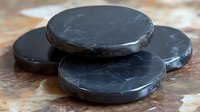 Black polished basalt hot stones for spa massage therapy arranged on marble surface, showing smooth texture and natural mineral properties for wellness treatments.