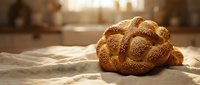 Fresh braided challah bread with sesame seeds on kitchen counter, golden crust glowing in warm sunlight, traditional Jewish bakery product for holidays.