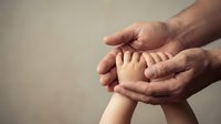 Adult hands gently holding baby feet in protective gesture showing care, love and family bond between parent and newborn child.