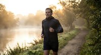 Athletic young man jogging along riverside path during golden hour sunrise workout session for healthy lifestyle and fitness motivation.