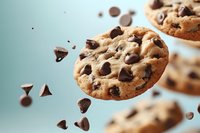 Freshly baked chocolate chip cookies with chunks flying through air, golden brown treats with melted chocolate pieces for bakery advertising and food marketing.