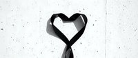 Black ribbon twisted into a heart shape against a light textured wall, monochrome style symbolizing love, mourning, or awareness campaigns.