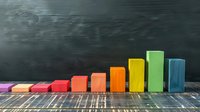 Colorful wooden blocks arranged as ascending bar graph on rustic wooden surface against dark chalkboard background, showing growth or progress concept.