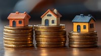 Small model houses placed on stacks of gold coins showing real estate investment, property market value, and housing costs concept on dark background.