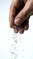 Close-up of male hands with medium skin tone sprinkling sea salt crystals against white background. Suitable for culinary, wellness, and food preparation concepts.
