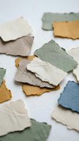 Handmade paper scraps in earthy tones scattered on white surface. Torn edges create organic texture for crafting, scrapbooking and artistic projects.