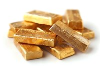Stack of shiny gold bullion bars scattered on white background, showing precious metal investment wealth and financial value concept with selective focus.