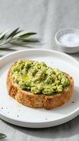 Fresh avocado toast on artisan bread with olive oil and black pepper seasoning served on white plate for healthy breakfast or brunch meal concept.