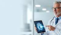 Senior Caucasian male doctor with glasses and stethoscope pointing at digital heart scan on tablet in modern medical office for cardiology consultation.