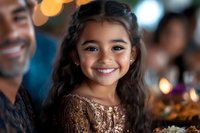 Young girl with radiant smile wearing sparkly bronze dress at celebration event, natural long dark hair styled with small braids, warm bokeh lighting background.