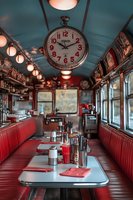 Interior of classic American diner with red leather booths, vintage wall clock, and retro lighting. Chrome details and table settings create nostalgic atmosphere.
