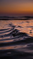 Ocean waves at sunset with golden orange sky reflecting on water surface creating peaceful seascape for meditation and relaxation backgrounds.
