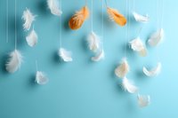 Delicate white and orange feathers floating against turquoise background create dreamy, ethereal composition for wellness, spirituality and lightness concepts.