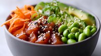 Fresh poke bowl with raw salmon, edamame beans, carrots, avocado and sesame seeds served in dark ceramic bowl on gray background.