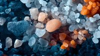 Macro shot of colorful salt crystals in blue, orange and white tones creating abstract mineral texture pattern with dramatic lighting and depth effect.