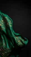 Luxurious emerald green silk fabric with golden embroidered floral patterns draped elegantly against dark background for premium fashion and textile design.