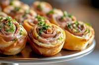 Savory puff pastry pinwheels filled with prosciutto and herbs, garnished with fresh parsley on metal serving plate, close up view of appetizing party snacks.