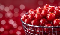 Fresh red currants covered with water drops in metal wire basket against blurred festive bokeh background, macro food photography.