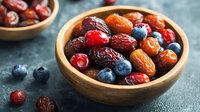 Fresh and dried berries mixed in wooden bowl on dark background, healthy organic superfood snack with cranberries, dates and blueberries for nutrition.