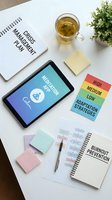 Business crisis management planning workspace with tablet showing meditation app, tea cup, colorful priority cards and burnout prevention notebook on white desk.
