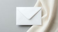 White envelope on elegant cream silk fabric background for luxury correspondence and wedding invitations.