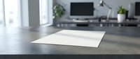 Clean white paper sheet on dark wooden desk in modern office workspace with computer monitor and plants in blurred background for business presentations.