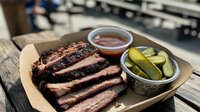 Smoked beef brisket slices with pink smoke ring, served with barbecue sauce and pickles on rustic wooden table. Traditional Texas-style BBQ platter.