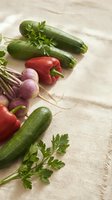 Fresh organic vegetables including zucchini, red bell pepper, purple radishes and parsley herbs arranged on natural linen fabric for healthy cooking and nutrition.