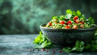 Fresh tabbouleh salad with parsley, tomatoes and bulgur wheat in dark stone bowl on rustic background, traditional middle eastern cuisine.