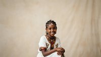 Young Black female child wearing white t-shirt and red beaded necklace, smiling at camera against neutral beige backdrop, suitable for educational, diversity, and family-themed projects.