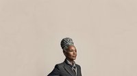 Mature African American female professional wearing dark blazer and striped tie against neutral beige background, suitable for corporate, business, and leadership concepts.