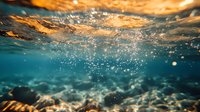 Dramatic split underwater view with golden sunset sky above and turquoise depths below, showing air bubbles and sunlight rays penetrating ocean surface.
