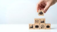 Hand placing wooden cube with paw print icon on stack of business symbol blocks representing team building and corporate growth strategy.