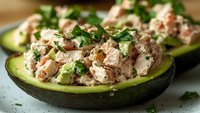 Stuffed avocado halves filled with tuna salad mixed with vegetables and fresh herbs, healthy low-carb meal option for lunch or dinner preparation.
