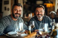 Middle-aged Caucasian men with gray beards enjoying dinner and wine at restaurant table, sharing genuine laughter and conversation during social gathering.