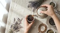 Woman hands preparing herbal tea with dried lavender flowers on linen tablecloth. Natural wellness ritual with organic ingredients and ceramic bowls.