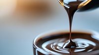 Dark chocolate sauce pouring in slow motion creating concentric ripples and circles, macro food photography with shallow depth of field on blurred background.