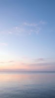 Serene ocean horizon at dawn with pastel sky in soft pink and blue hues reflecting on calm water surface creating peaceful seascape atmosphere.