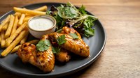 Grilled chicken breast with golden french fries, fresh mixed greens salad and creamy dipping sauce served on dark plate for restaurant menu photography.