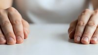Woman hands placed flat on white surface showing natural skin tone and manicured nails for wellness and self-care concepts.