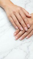 Hands of a woman with light skin tone displaying a classic French manicure with soft pink nail beds and white tips on marble surface. Suitable for beauty, nail care, cosmetics, and wellness marketing.