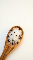 Wooden spoon filled with sea salt crystals and black peppercorns on neutral background, suitable for culinary, food styling, and cooking-related projects.