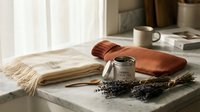 Cozy home spa setup with lavender candle, soft towels and dried flowers on marble surface creating relaxing wellness atmosphere for self-care rituals.