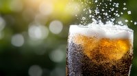 Cold carbonated cola drink with ice cubes in glass against blurred green bokeh background, refreshing beverage with bubbles and foam splashing.