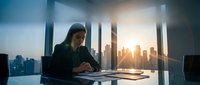 Professional businesswoman working at modern office desk with city skyline view during golden hour sunset, corporate lifestyle and career success.