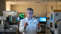 Middle-aged Caucasian male scientist in white lab coat examining digital holographic display in modern laboratory with advanced equipment and technology.