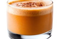 Creamy pumpkin spice latte topped with frothy milk foam and dusted cinnamon in glass cup against white background, autumn beverage photography.