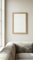 Blank wooden frame mockup on beige wall above linen sofa in minimalist Scandinavian living room interior with natural light.